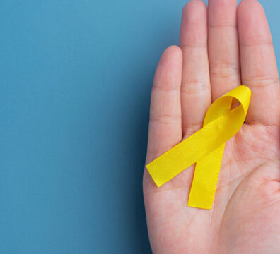 Hands holding yellow ribbon, symbol of cancer awareness, medical support and prevention with helping hand. Suicide prevention day concept